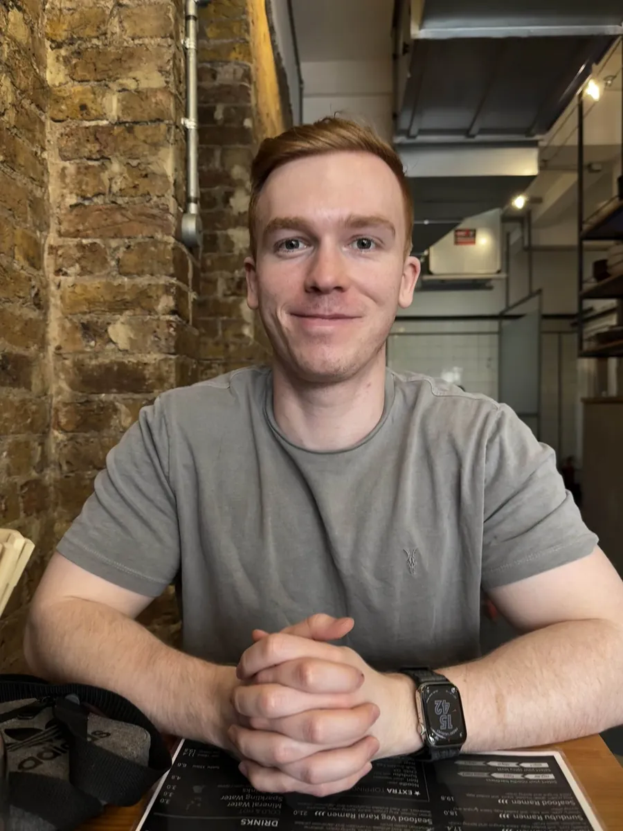 Matthew smiling, seated at a table with his hands clasped